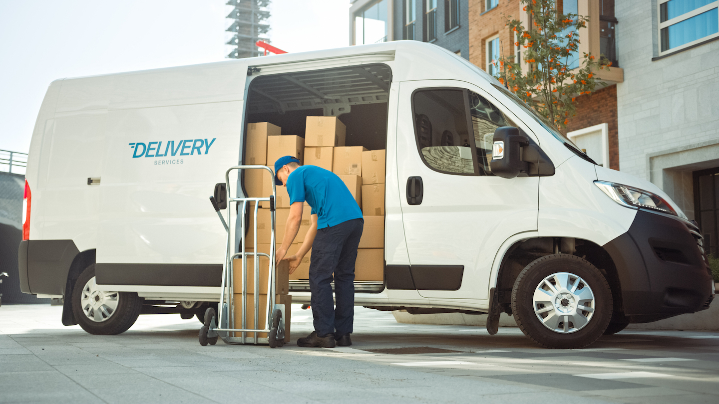 Courier Takes out Cardboard Box Package From Opened Delivery Van Side Door. Professional Courier / Loader helping you Move, Delivering Your Purchased Items Efficiently. GD Rectifiers Delivery & Collection Options. Packaging solutions by GD Rectifiers.